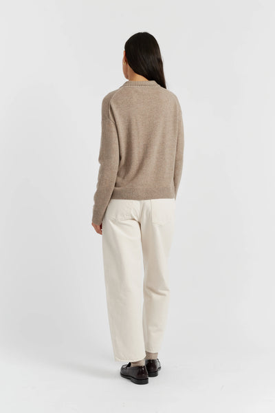 Person wearing a brown sweater and white pants on a white background