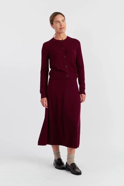 Woman wearing a burgundy cardigan and skirt set on a white background