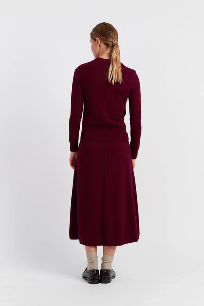 Woman wearing a burgundy outfit with a long skirt on a white background