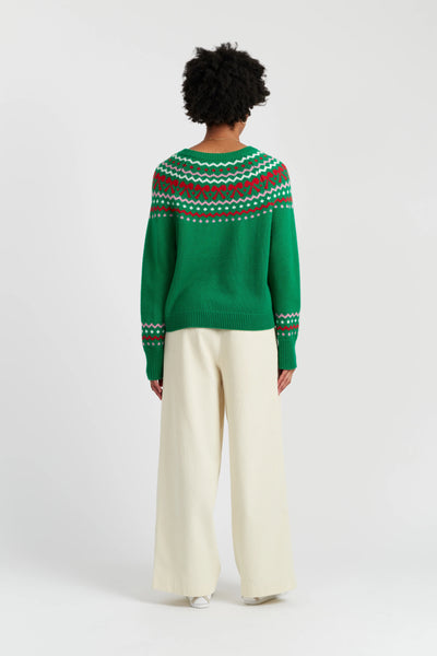 Person wearing a green sweater with a pattern, standing against a white background