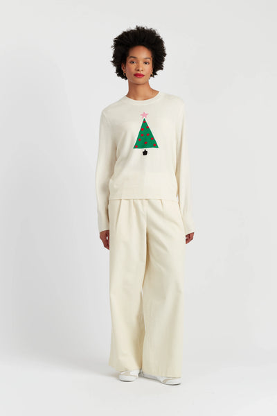 Person wearing a cream sweater with a Christmas tree design and matching pants on a white background