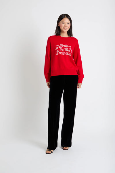 Person wearing a red sweater with text and black pants on a white background