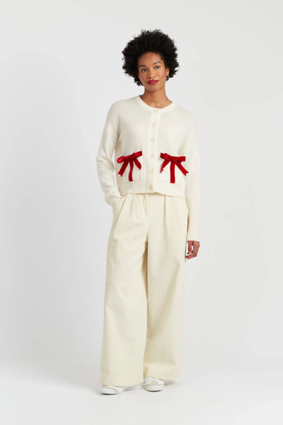 Person wearing a cream outfit with red bow details on a white background