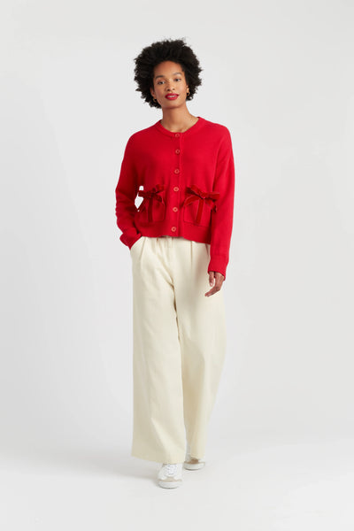 Person wearing a red cardigan and beige pants on a white background