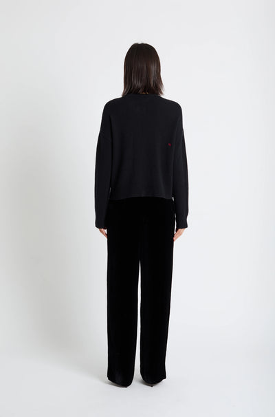 Person wearing a black outfit with a red heart detail on a white background