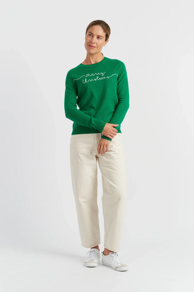 Person wearing a green 'Merry Christmas' sweater with white pants on a white background