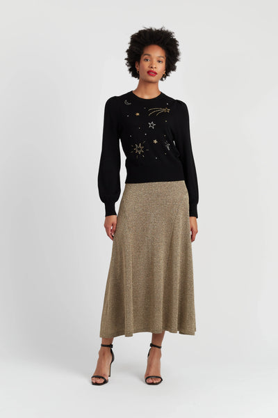 Woman wearing a black sweater with gold designs and a beige skirt on a white background