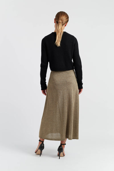 Woman wearing a black top and long beige skirt on a white background