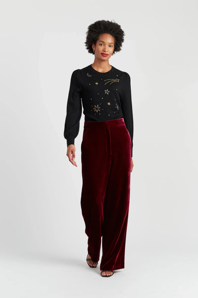Woman wearing a black sweater with star patterns and red velvet pants on a white background