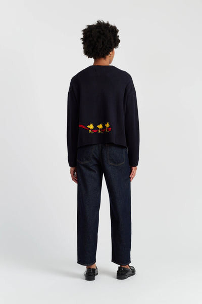 Person wearing a black sweater with colorful designs on the back, standing against a white background