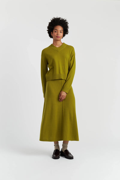 Person wearing a green sweater and skirt set on a white background