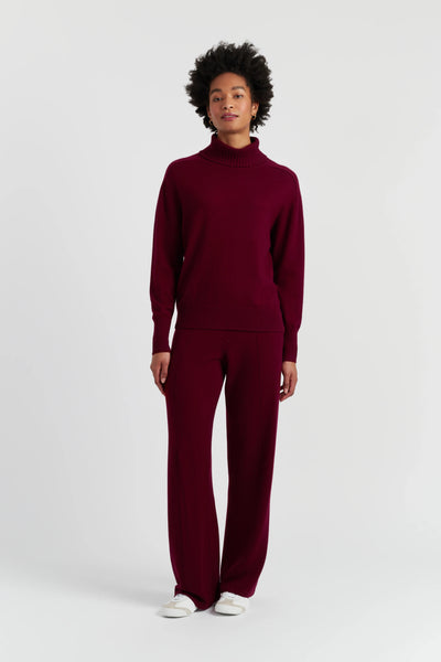 Person wearing a burgundy turtleneck sweater and pants on a white background