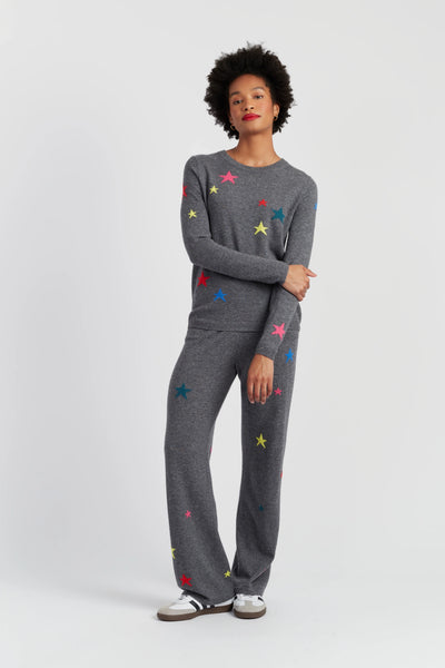 Woman wearing a gray sweater and pants with colorful star patterns on a white background