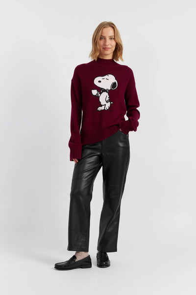 Woman wearing a burgundy sweater with a graphic design, black pants, and black shoes on a white background
