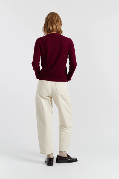 Person wearing a burgundy sweater and white pants on a plain background