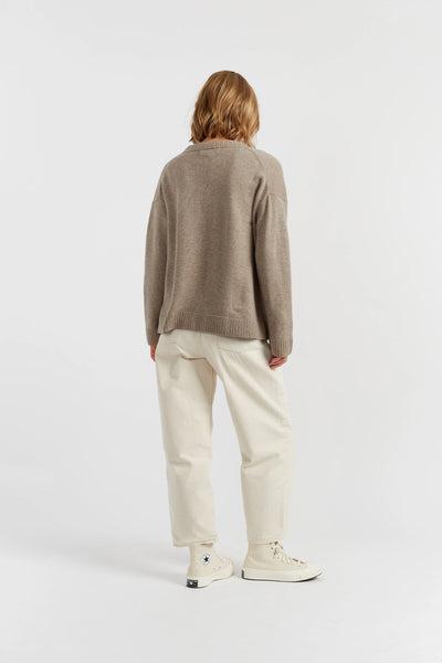 Person wearing a brown sweater and beige pants on a white background