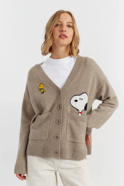 Woman wearing a beige cardigan with cartoon character patches on a white background
