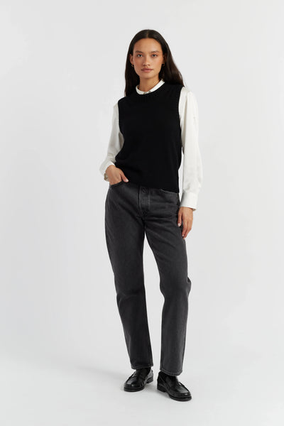 Person wearing a black sleeveless top, white long-sleeve shirt, gray pants, and black shoes on a white background