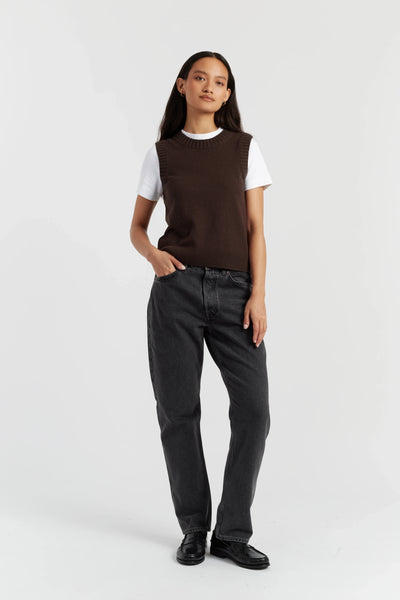 Person wearing a brown vest over a white shirt with black pants on a white background