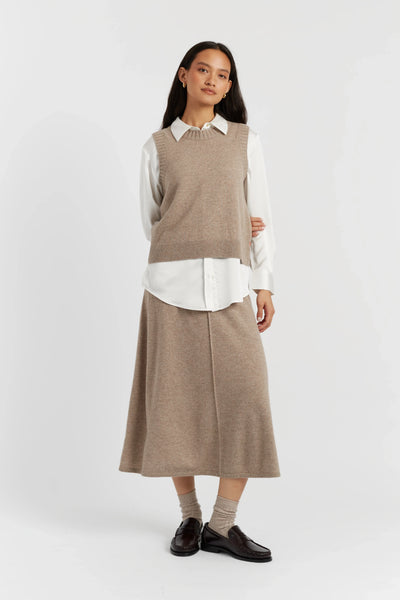 Woman wearing a beige knitted vest over a white shirt with a matching skirt on a white background
