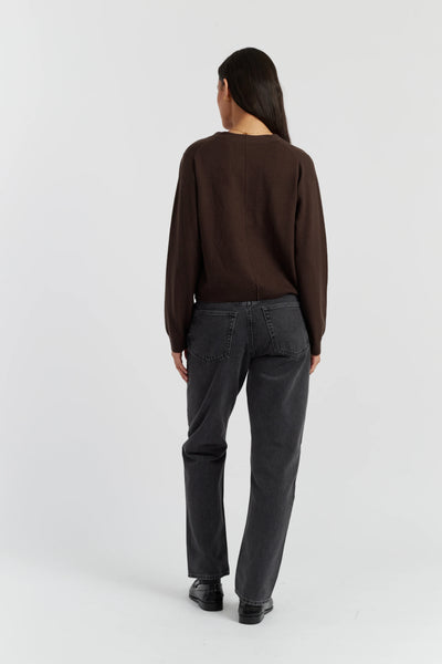 Person wearing a brown sweater and dark gray pants on a white background