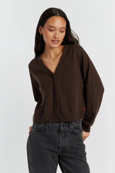 Woman wearing a brown cardigan and dark jeans on a white background