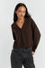 Woman wearing a brown cardigan and dark jeans on a white background