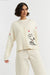 Woman wearing a cream cardigan with a cartoon character design on a white background
