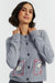 Woman wearing a gray cardigan with embroidered designs on a white background