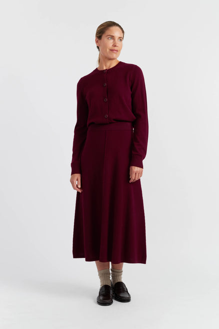 Woman wearing a burgundy outfit with a sweater and skirt on a white background