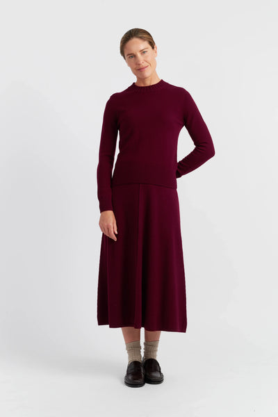 Woman wearing a burgundy long-sleeve top and skirt on a white background