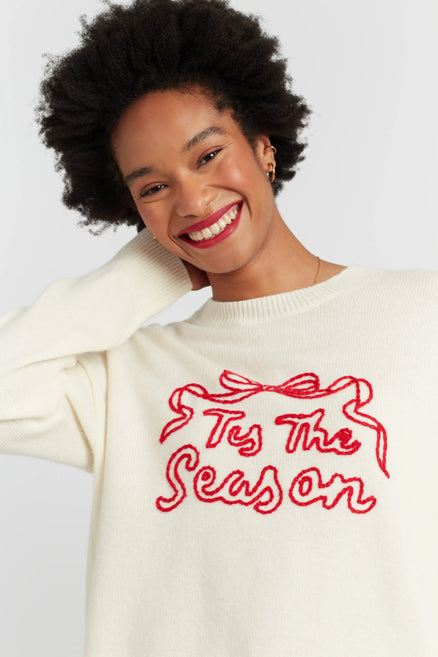 Woman wearing a cream sweater with 'Tis The Season' text in red on a white background