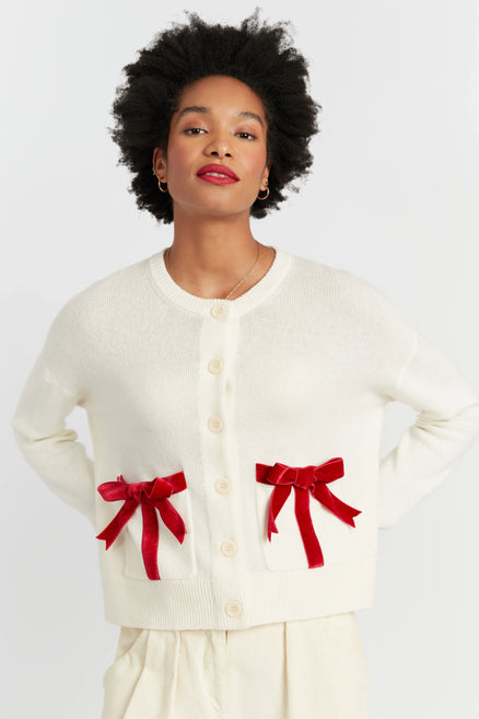 Woman wearing a cream cardigan with red bows on a white background