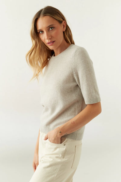 Woman wearing a light gray top and white pants on a white background