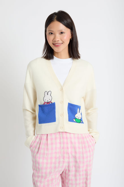 Woman wearing a cream cardigan with cartoon character patches on a white background