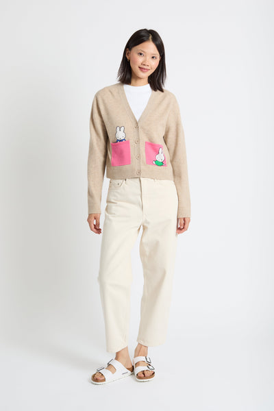 Woman wearing a beige cardigan with cartoon character pockets on a white background
