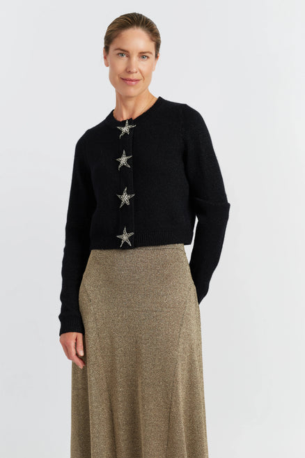 Woman wearing a black cardigan with star embellishments and a beige skirt on a white background
