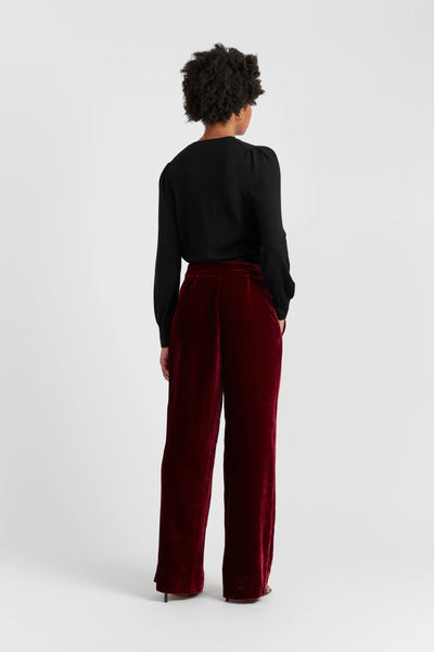 Person wearing a black top and burgundy pants on a white background