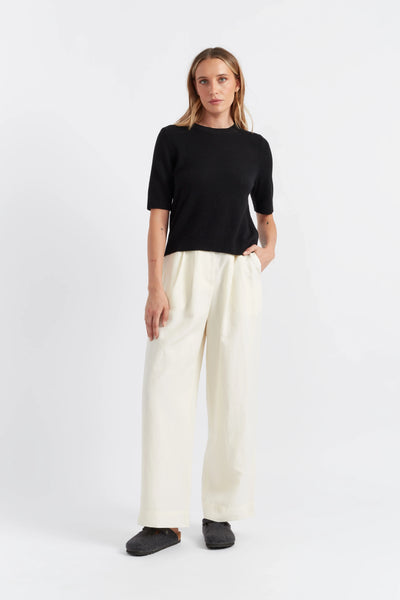 Woman wearing a black top and white pants on a white background