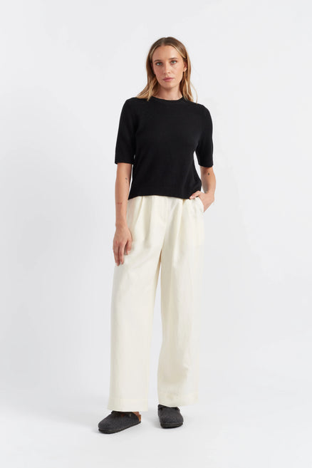 Woman wearing a black top and white pants on a white background