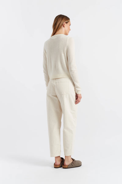 Woman wearing a beige sweater and pants against a white background