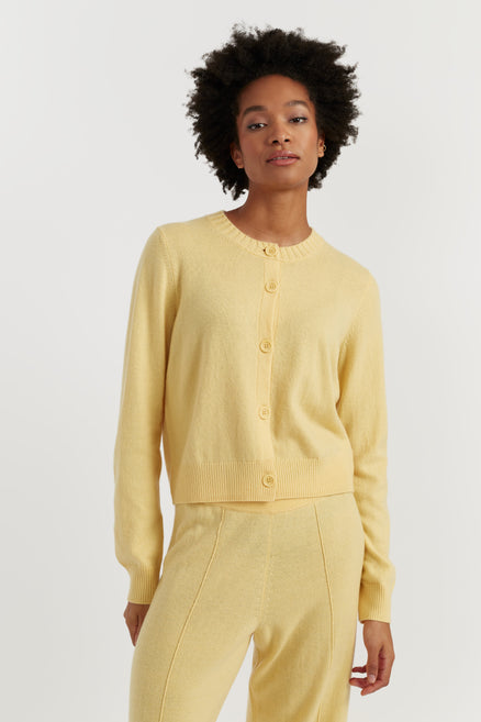 Woman wearing a yellow cardigan and pants against a white background