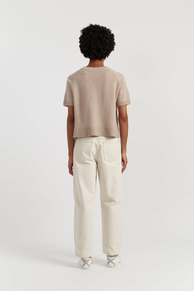 Person wearing a beige sweater and white pants on a white background