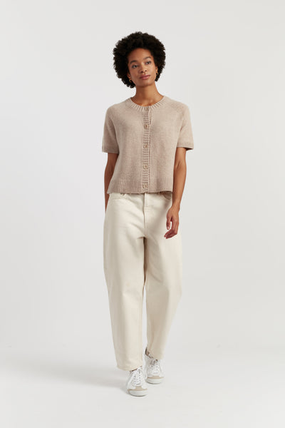 Person wearing a beige knit top and white pants on a white background