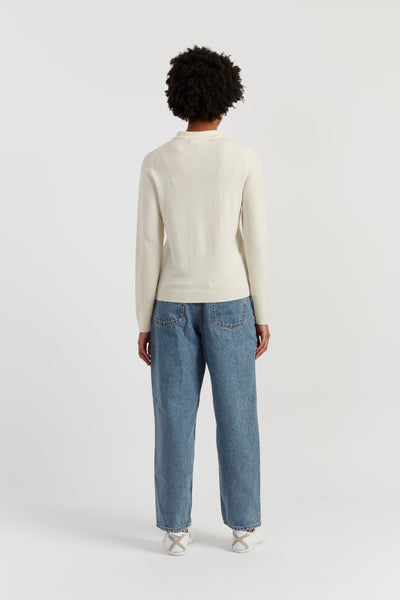 Person wearing a cream sweater and blue jeans on a white background
