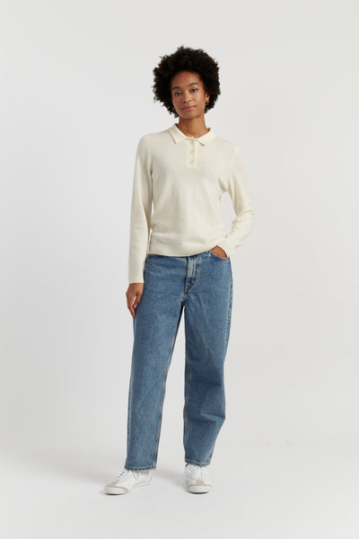 Person wearing a cream long-sleeve polo shirt and blue jeans on a white background