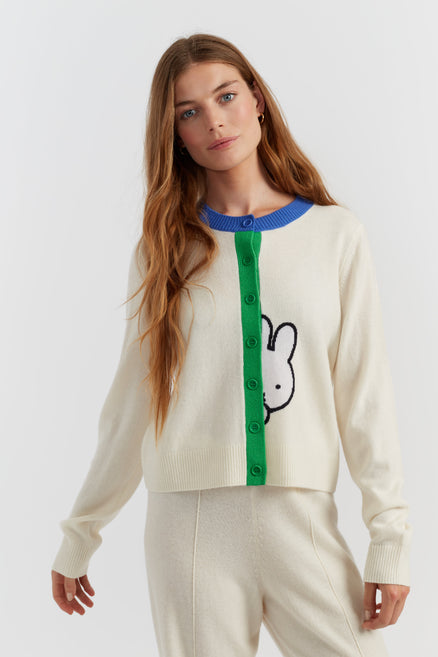 Woman wearing a cream sweater with a green and blue design on a white background