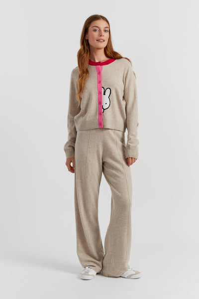 Woman wearing a beige and red sweater with a bunny logo, standing against a white background