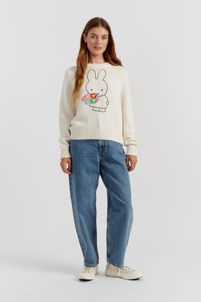 Woman wearing a sweater with a bunny design and blue jeans on a white background