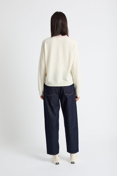 Person wearing a cream sweater and dark blue jeans on a white background